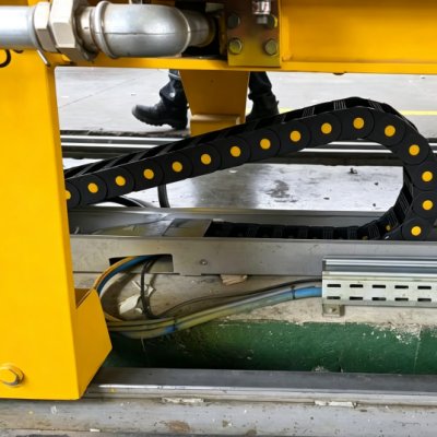 Yellow machinery base with plastic cable carrier chain in metal guide trough