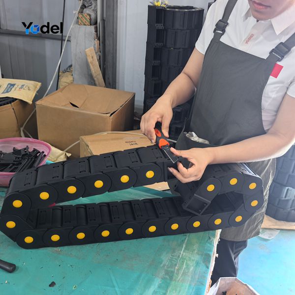 Factory worker inspecting link hinges and trimming snap covers on an assembled enclosed cable and hose carrier 80x150