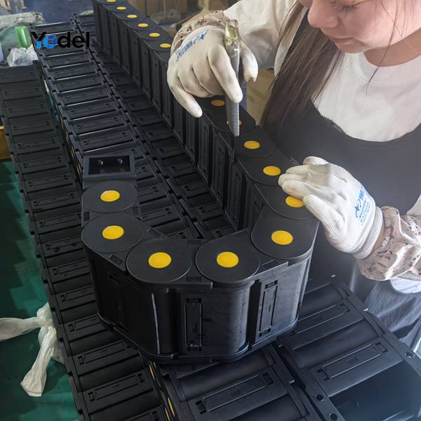 Factory workers assembling links and yellow side pins for cable drag chain 55x150 on production workbench