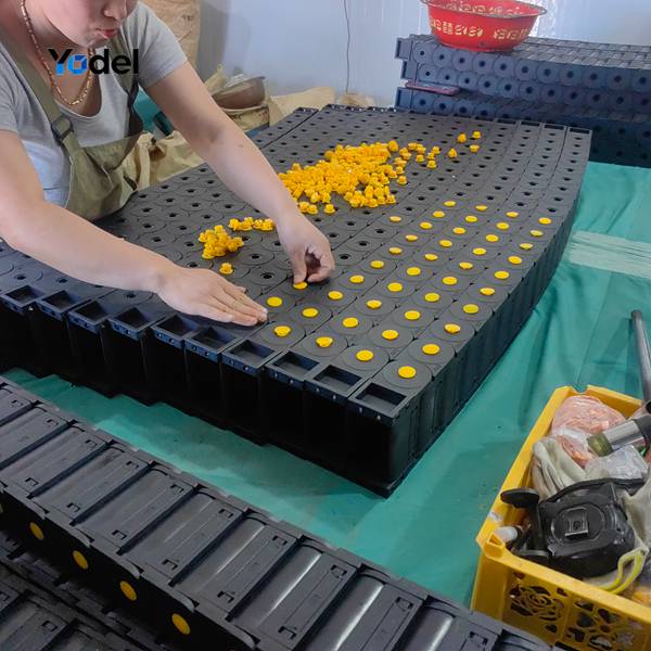 Skilled factory technician assembling links and yellow side pins for cable & hose carriers 65x125 on production table
